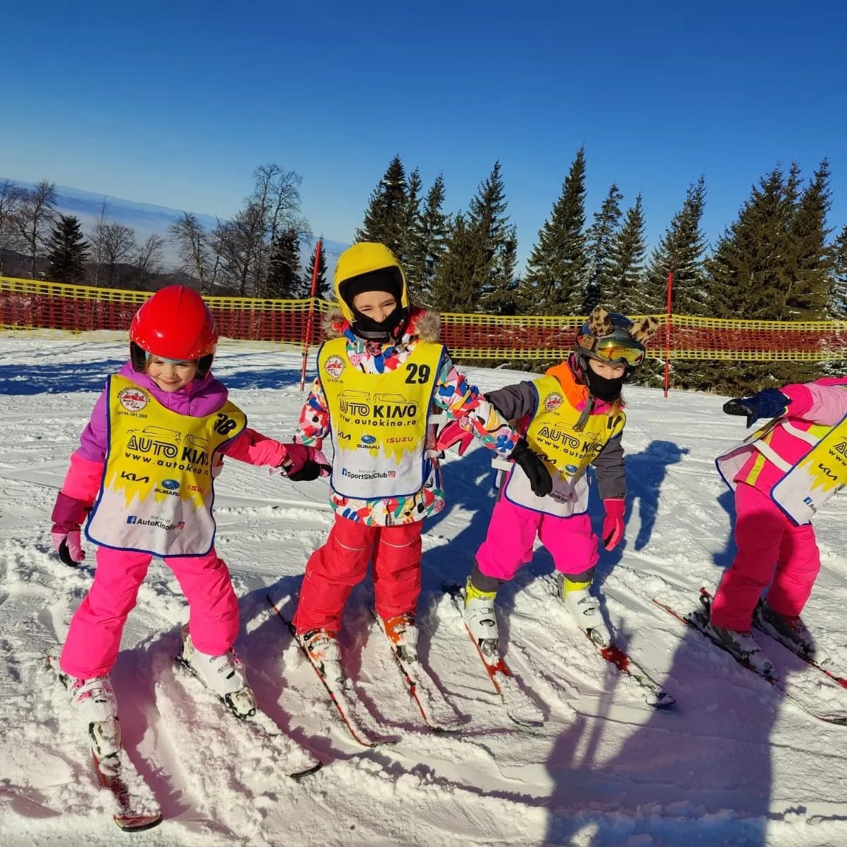 Grup de copii pe schiuri, în veste galbene, într-o zi senină